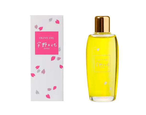 ピンク色の桜の花びらが散りばめられた白い化粧箱と、ゴールドのキャップがついた鮮やかな黄色の『宇野千代ブランド オリーブオイル』のボトル