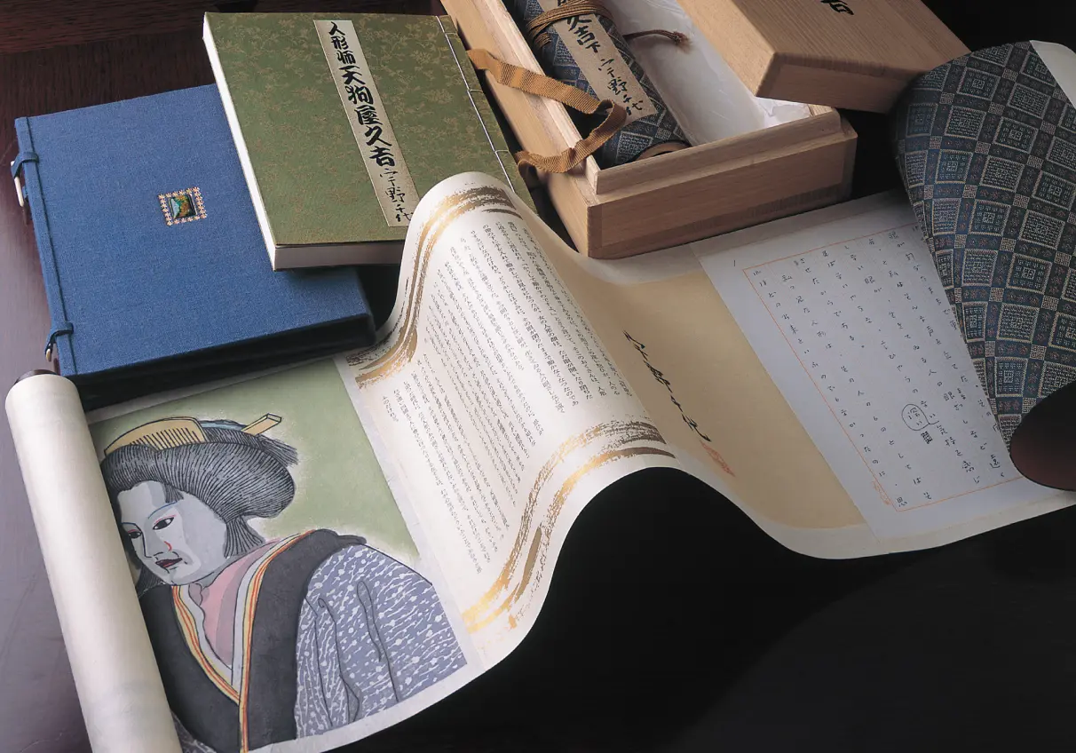 宇野千代の著書『人形師天狗屋久吉』の和装本や直筆原稿、広げられた美しい巻物と木箱のセット