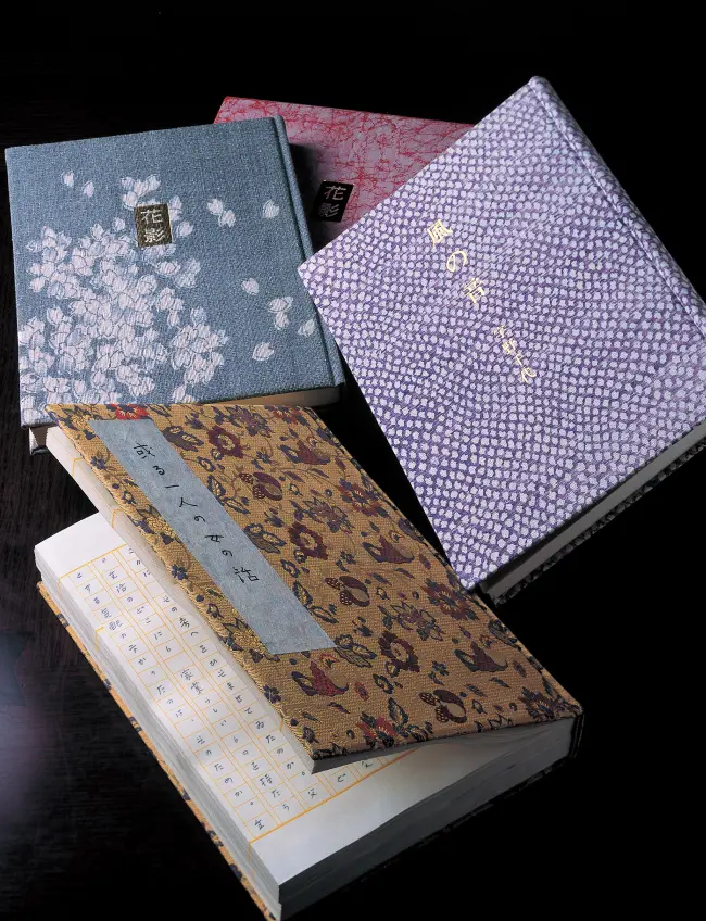 『花影』や『風の音』など、豪華な和柄の装丁が施された宇野千代の複数の和装本と開かれた書籍の重ね置き