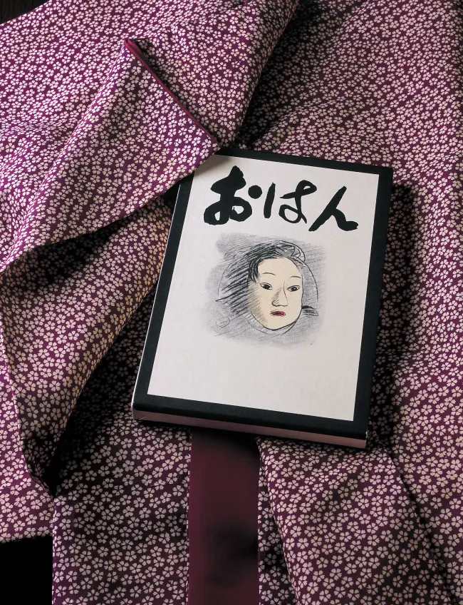 紫色の小桜模様の着物の手法の上に置かれた、女性の顔のイラストが描かれた宇野千代の小説『おはん』の書籍