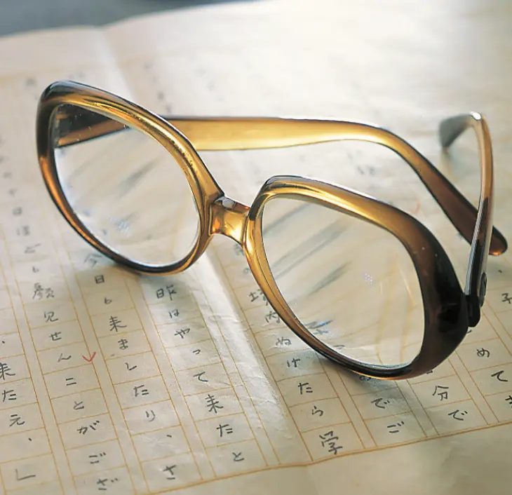 縦書きの文字と推敲の跡が残る直筆の原稿用紙の上に、光を反射して置かれた、宇野千代愛用の大きなべっ甲風の丸眼鏡のアップ写真