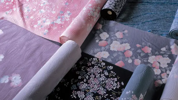 流れるような波紋の地ざらしに、可憐なピンクの桜や白い椿、夜桜を思わせる黒地に桜の文様など、華やかでモダンな色彩の着物の反物が美しく広げられ並ぶテキスタイル