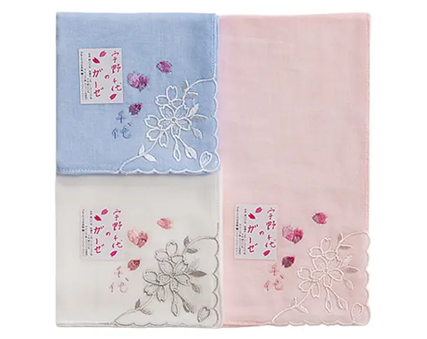 ブルー、ホワイト、ピンクの3色の『宇野千代のガーゼハンカチ』。角に白い糸で上品な桜の刺繍が施され、桜の花びらがあしらわれた商品タグが添えられている